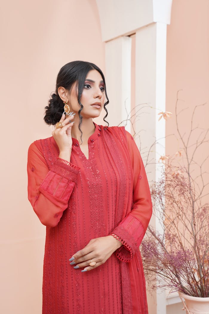 Woman in elegant traditional red dress posing indoors with an artistic touch.