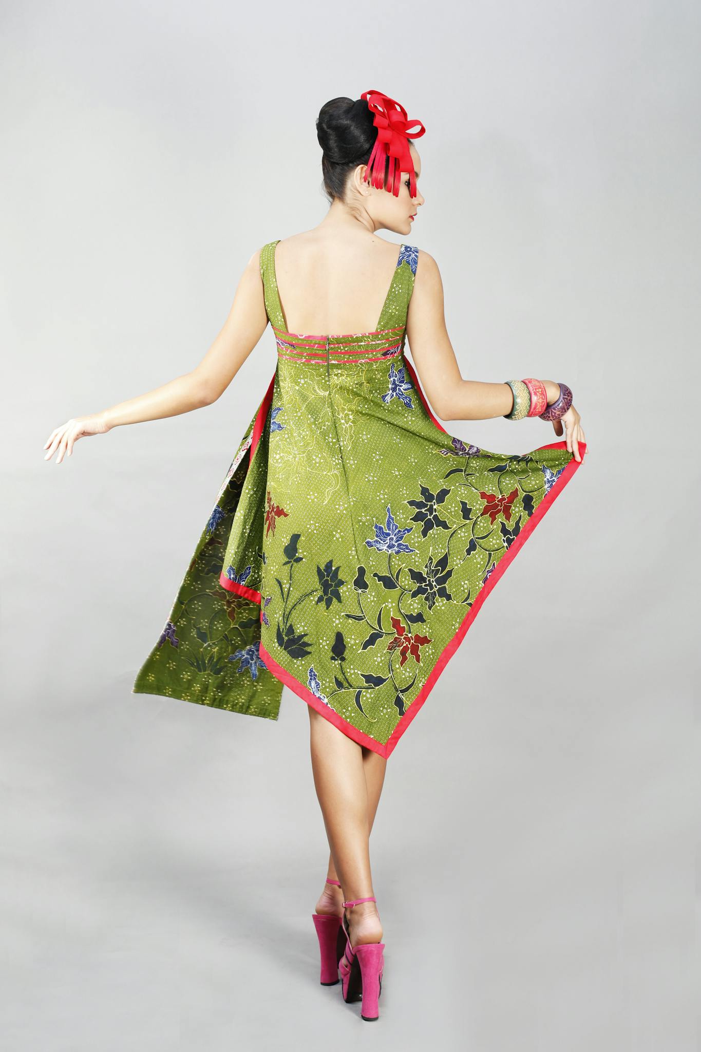 Stylish woman posing in a vibrant green batik dress with floral patterns, captured in a professional studio shoot.