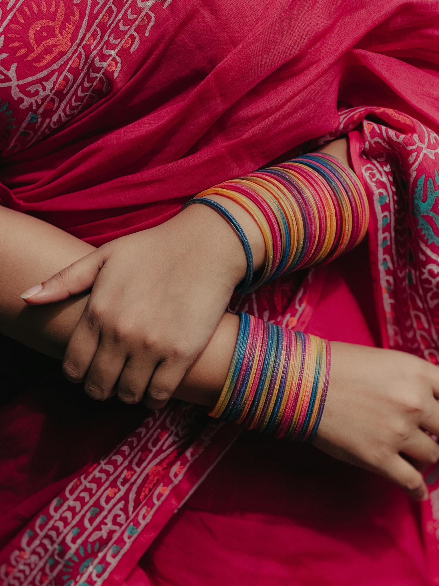 Vibrant multicolored bangles on a woman's arms, wrapped in a traditional red saree.
